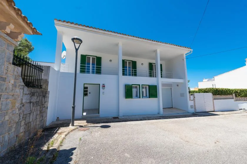A white two-story building with green shutters faces a paved courtyard.