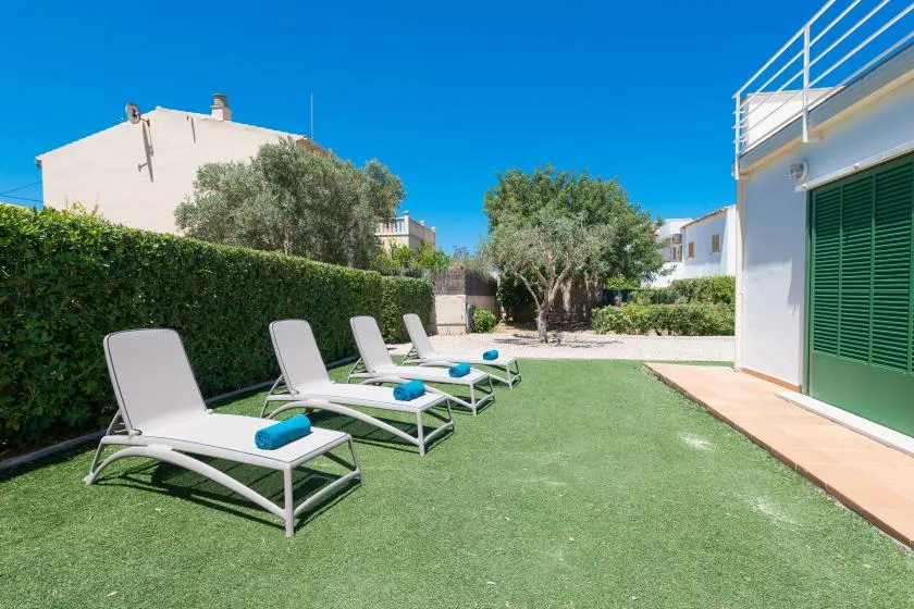 Outdoor seating area with sun loungers on a grassy patio beside a white building.
