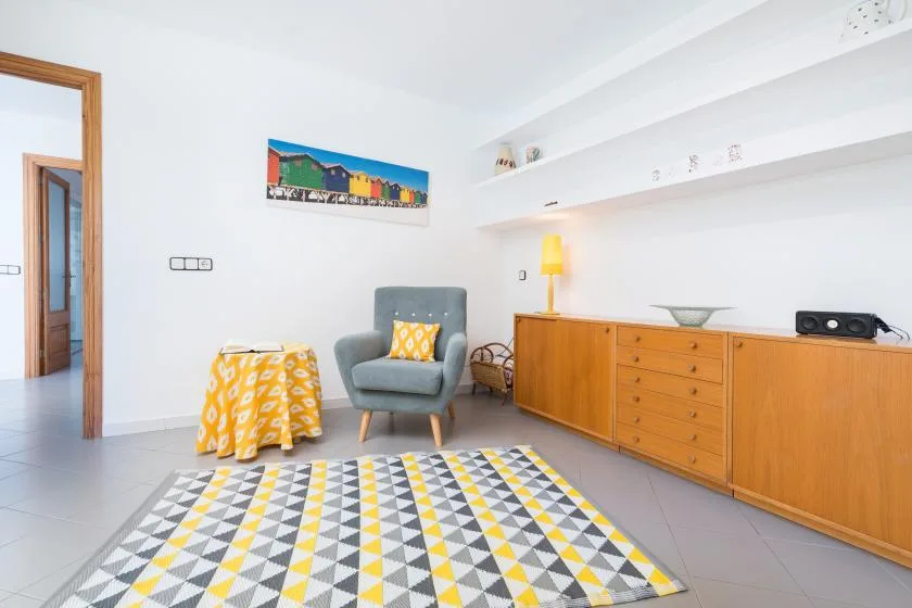 A bright living room with an armchair, patterned rug, and wooden cabinets.