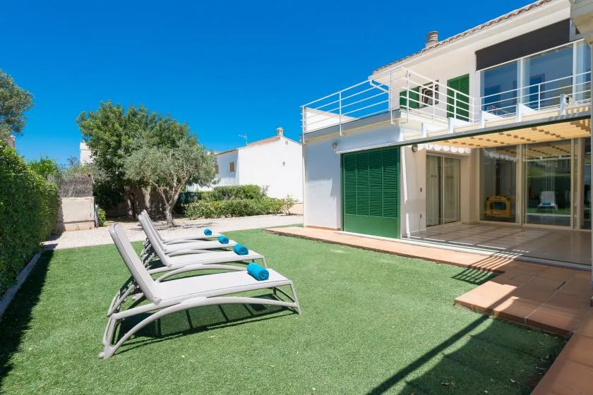 A sunny outdoor patio with reclining seating beside a modern house.