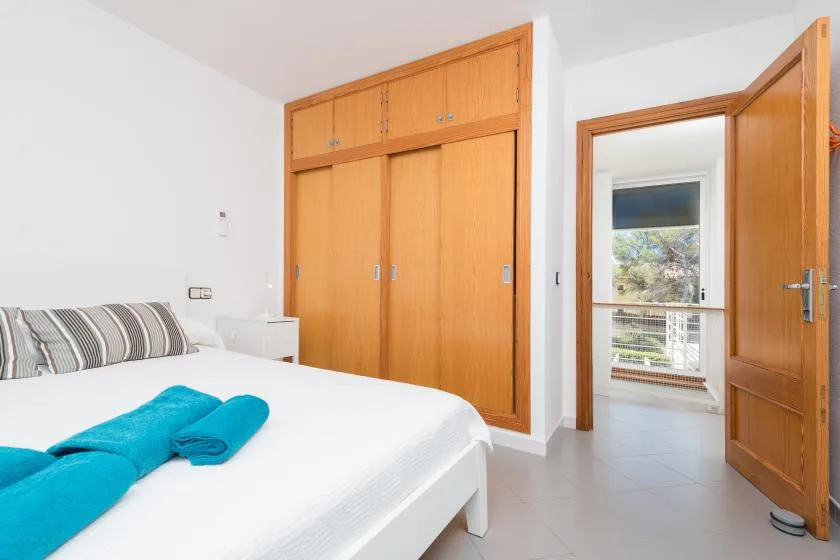 A bright bedroom with a bed, folded towels, and wooden wardrobes.