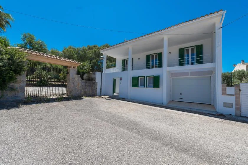 A modern two-story house stands beside a paved driveway and gated entrance.