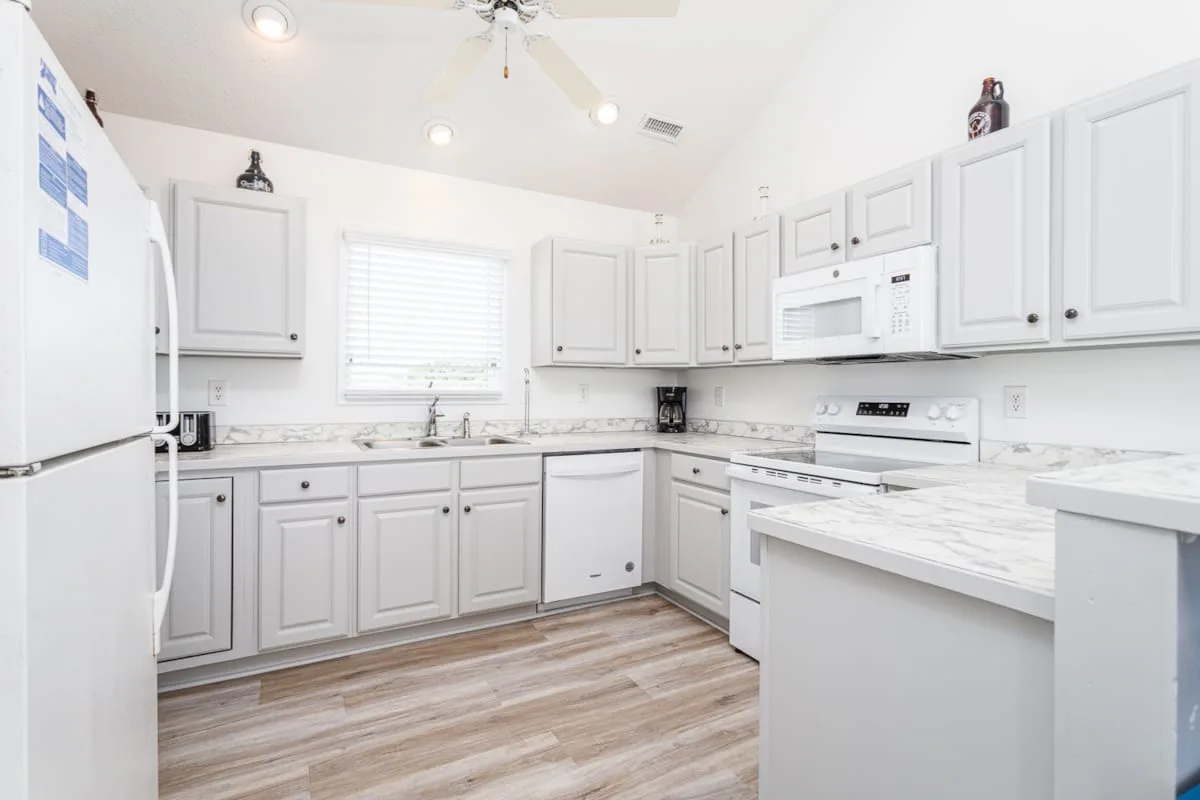 Una cocina luminosa con gabinetes blancos, electrodomésticos e isla central.