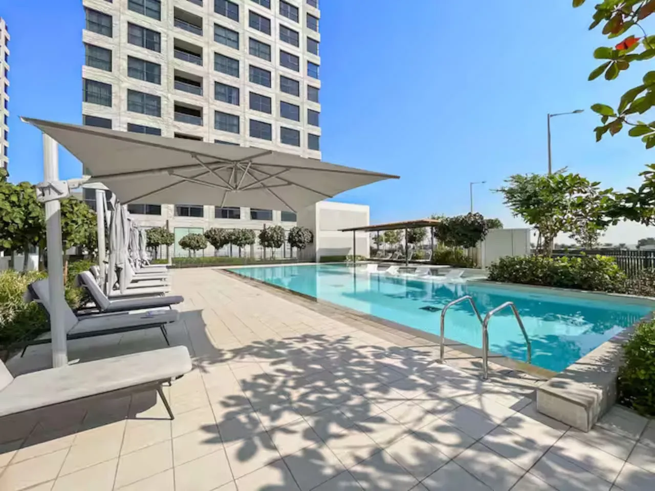 An outdoor swimming pool beside a tiled deck with lounge seating and a shade canopy.