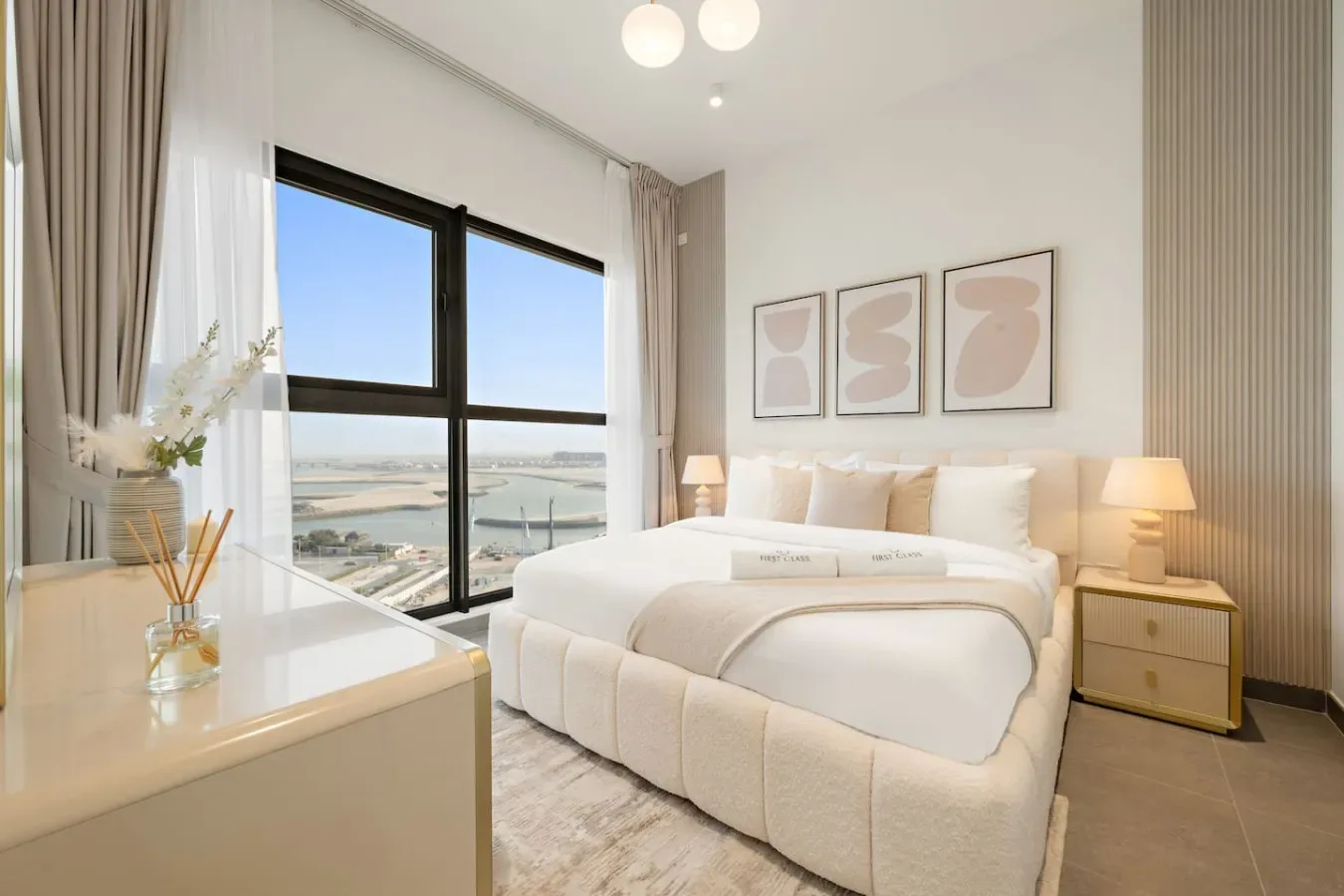 Un dormitorio luminoso con una cama bien tendida junto a grandes ventanas con vistas al agua.