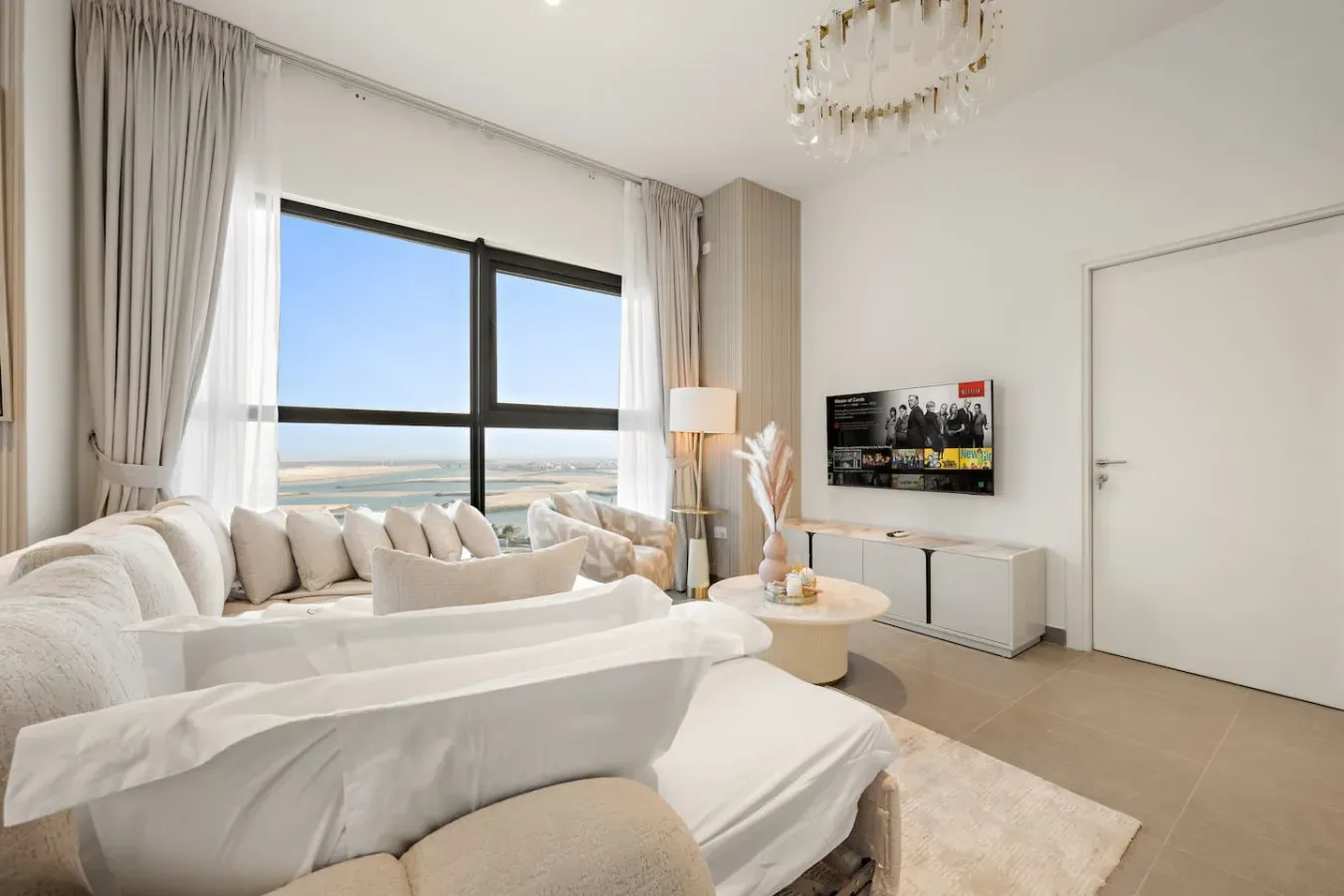 A bright living room with seating beside large windows overlooking the water.