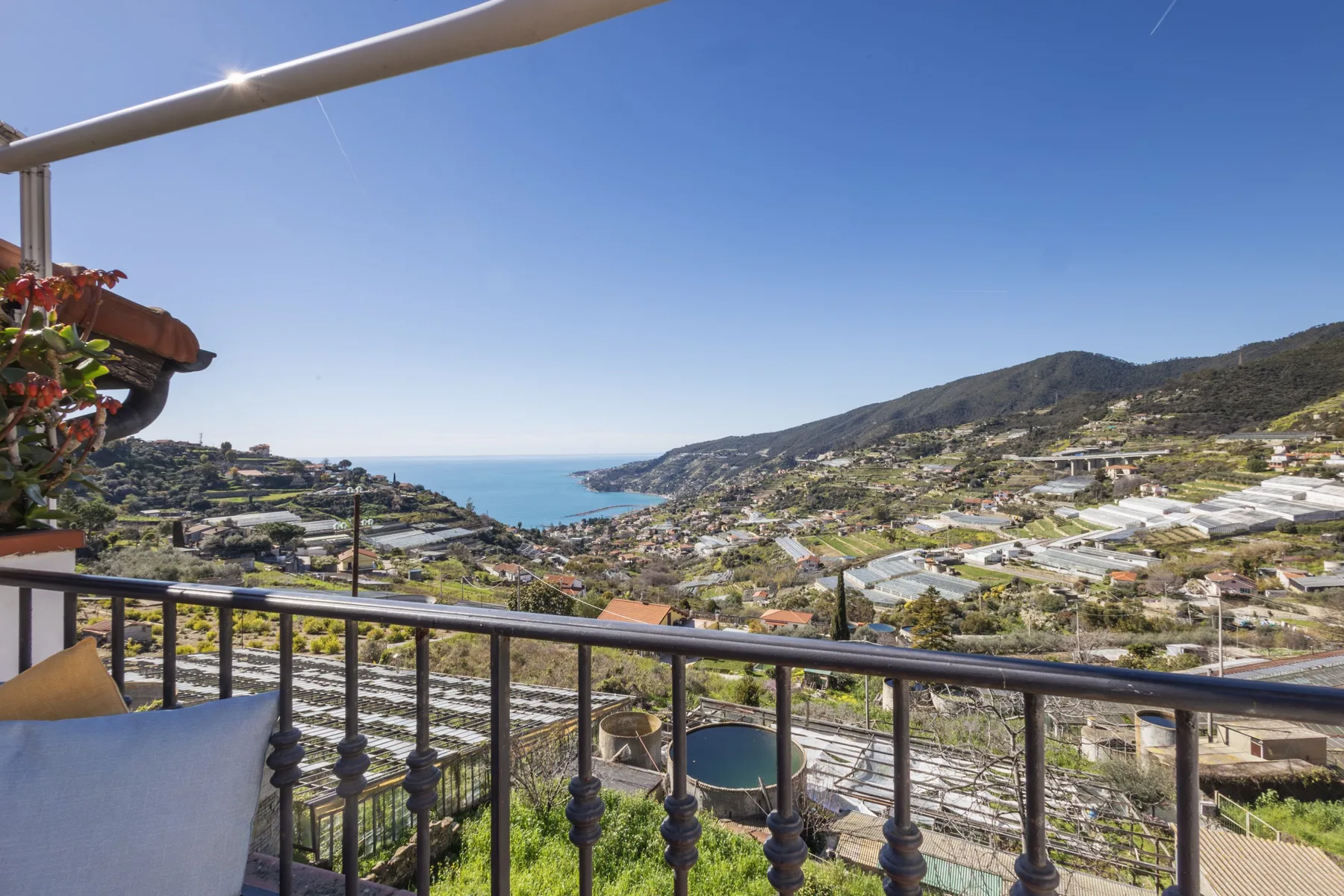 A balcony overlooks a coastal town and bay beneath a clear blue sky.