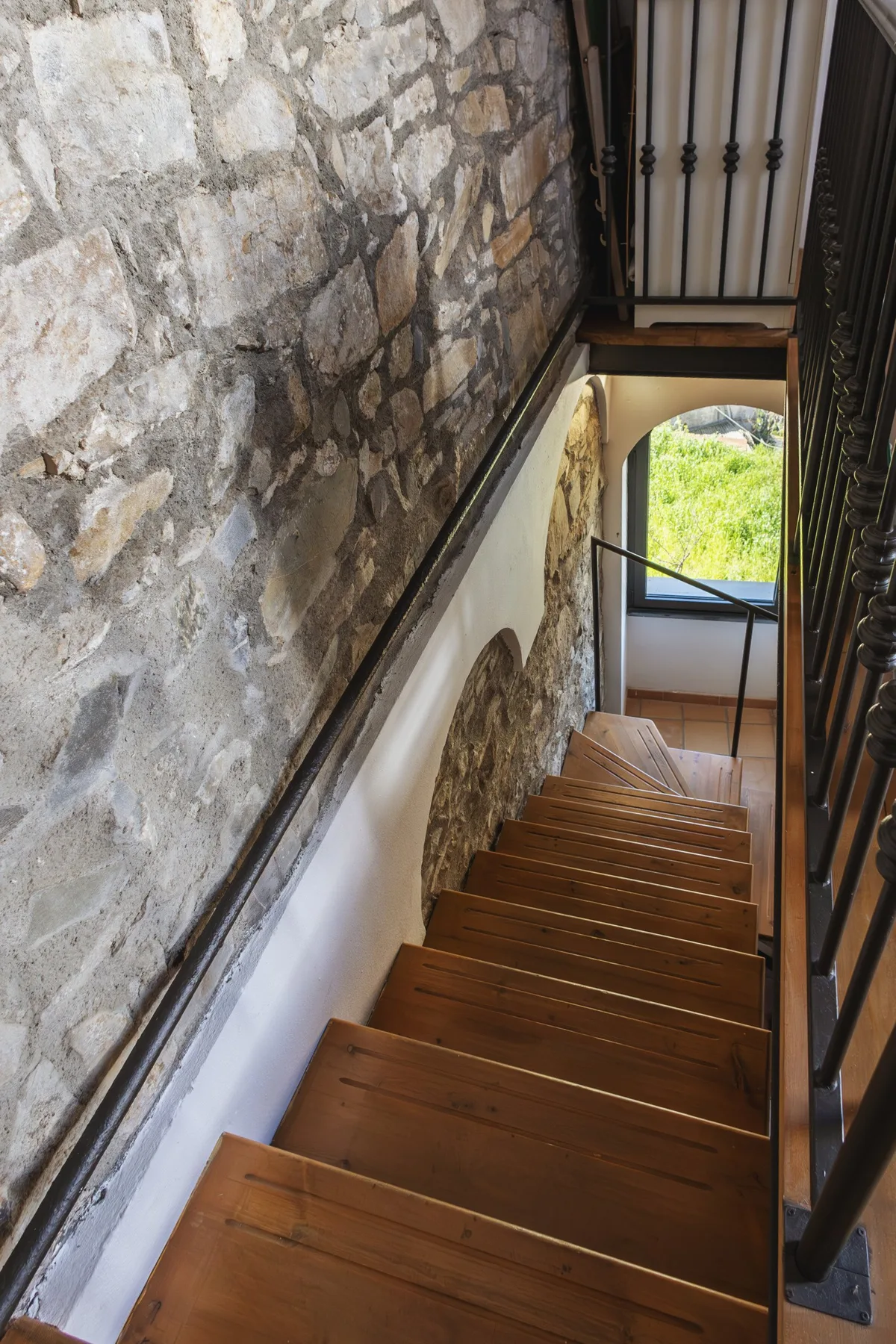 A wooden staircase descends beside an exposed stone wall and dark railing.