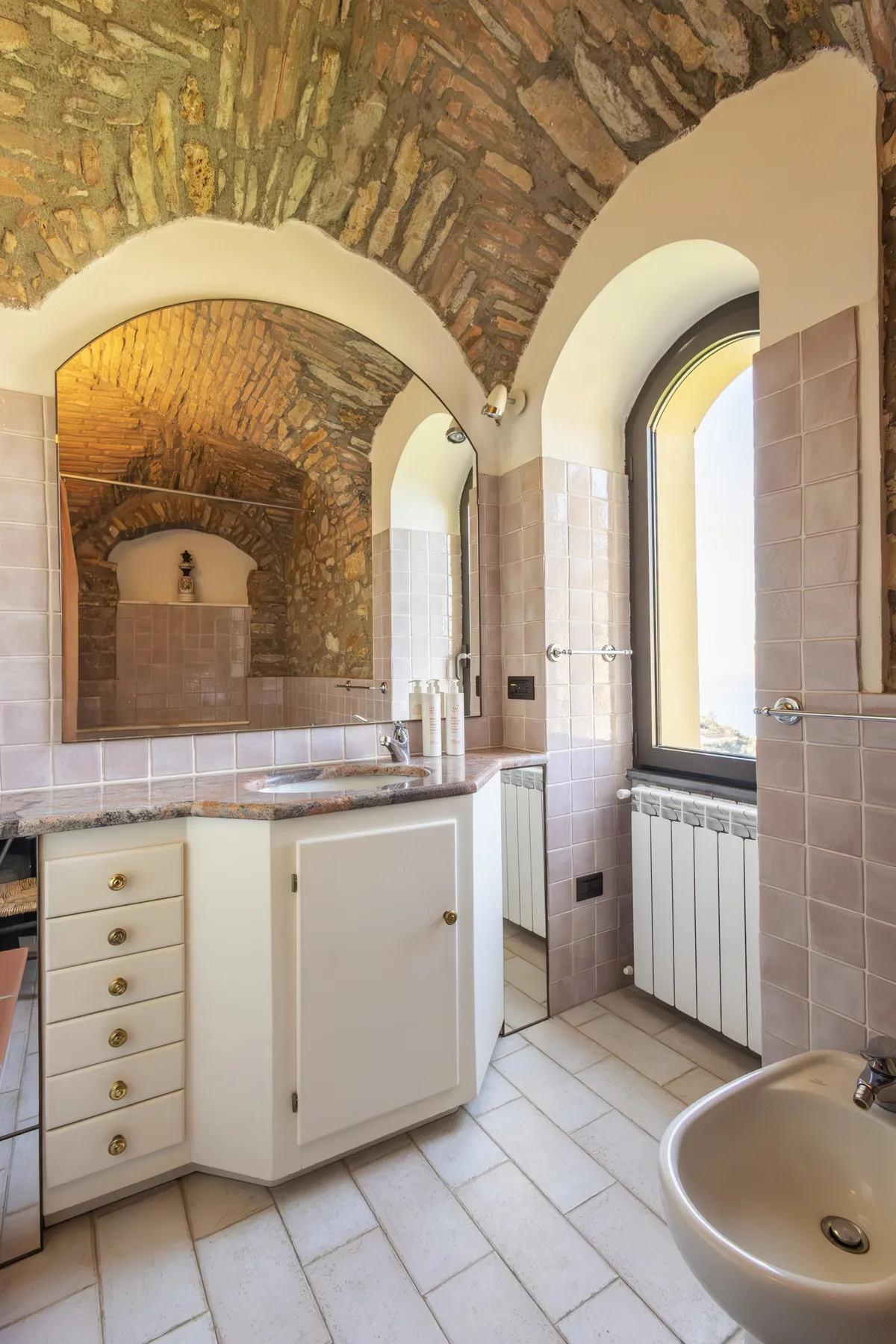 A bathroom with a sink vanity beneath arched windows and a brick ceiling.