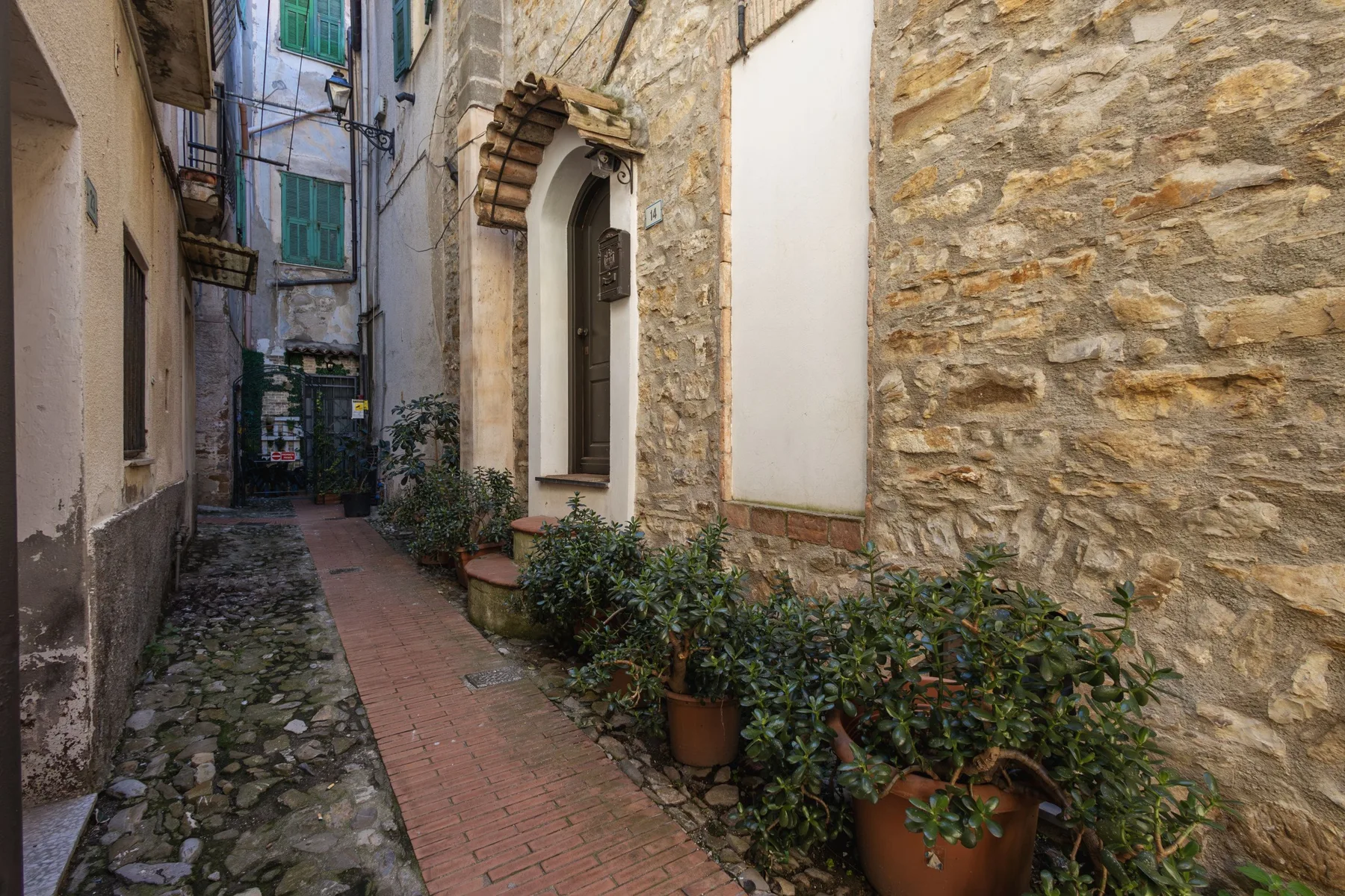 A narrow stone passage with a brick walkway and potted plants.