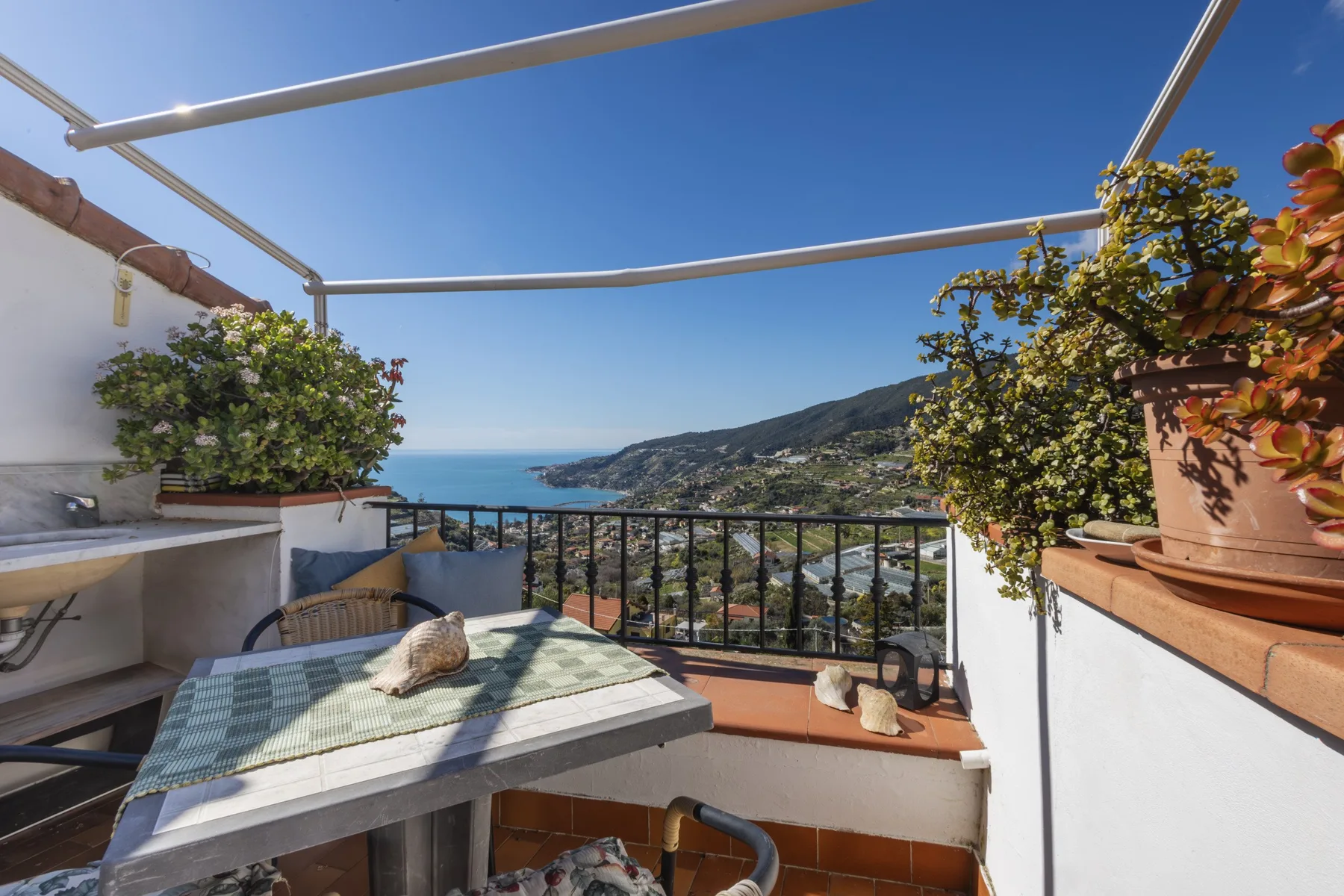 A sunny terrace overlooks the sea and a coastal hillside.