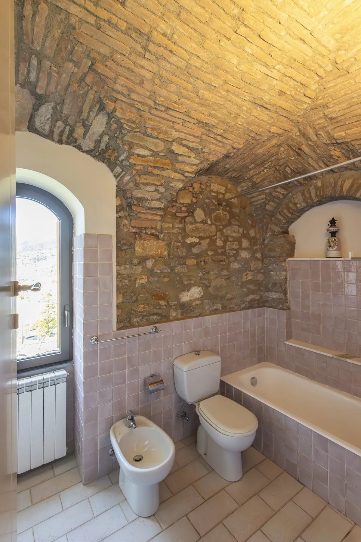 A tiled bathroom with a bathtub, toilet, and exposed brick ceiling.
