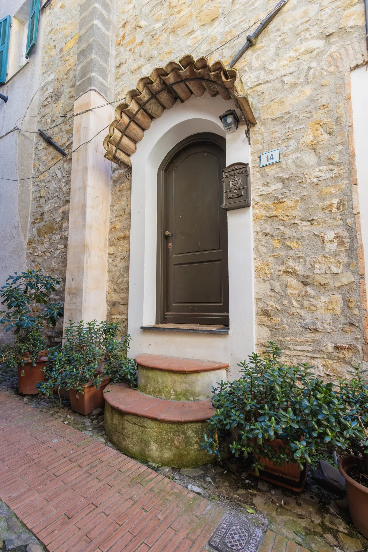 A stone building entrance with an arched doorway and potted plants along the walkway.
