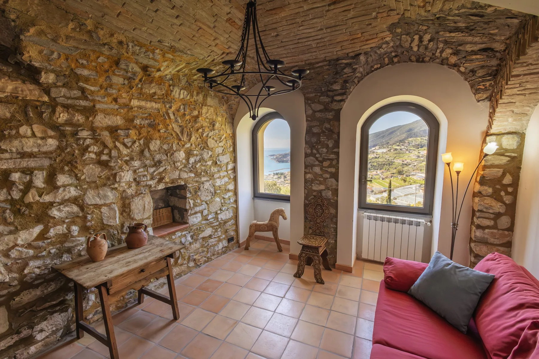 A rustic stone living room with arched windows and a red sofa.