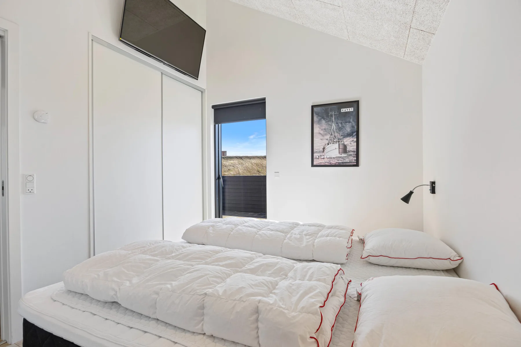Un dormitorio luminoso con ropa de cama blanca y una ventana con vistas a un terreno abierto.