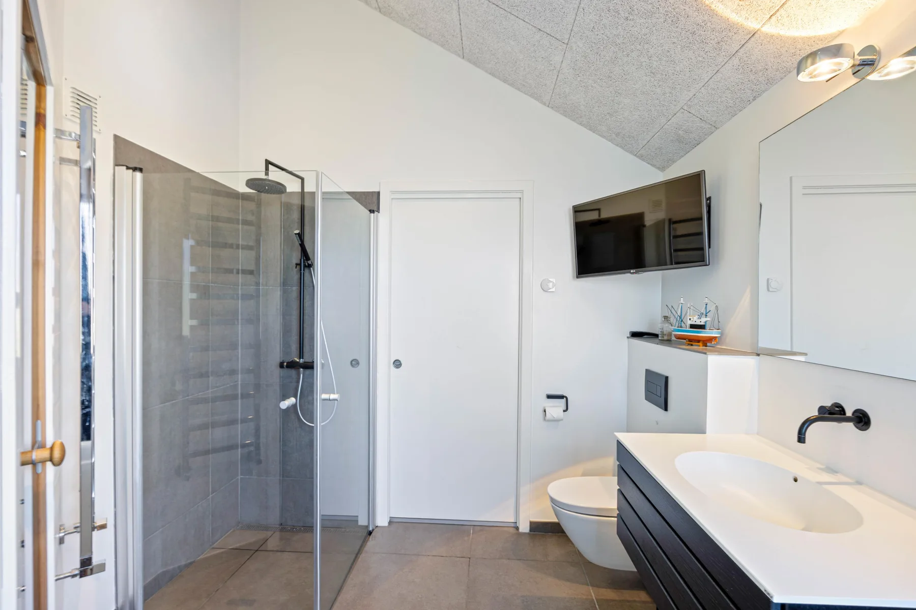 Baño moderno con ducha, inodoro y lavabo bajo un techo inclinado.