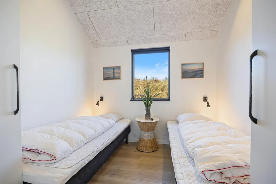 Un dormitorio luminoso con dos camas a los lados de una pequeña mesa bajo una ventana.
