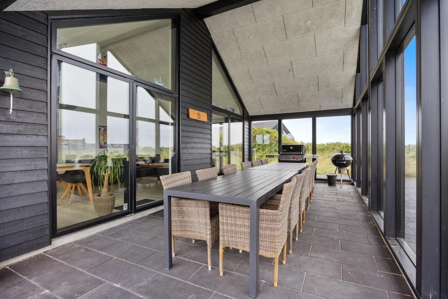 Comedor exterior cubierto con una mesa larga junto a grandes puertas de vidrio.
