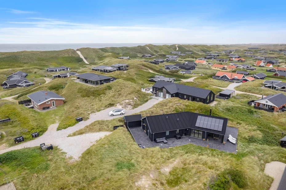Una vista aérea muestra casas dispersas entre dunas cubiertas de hierba bajo un cielo azul.