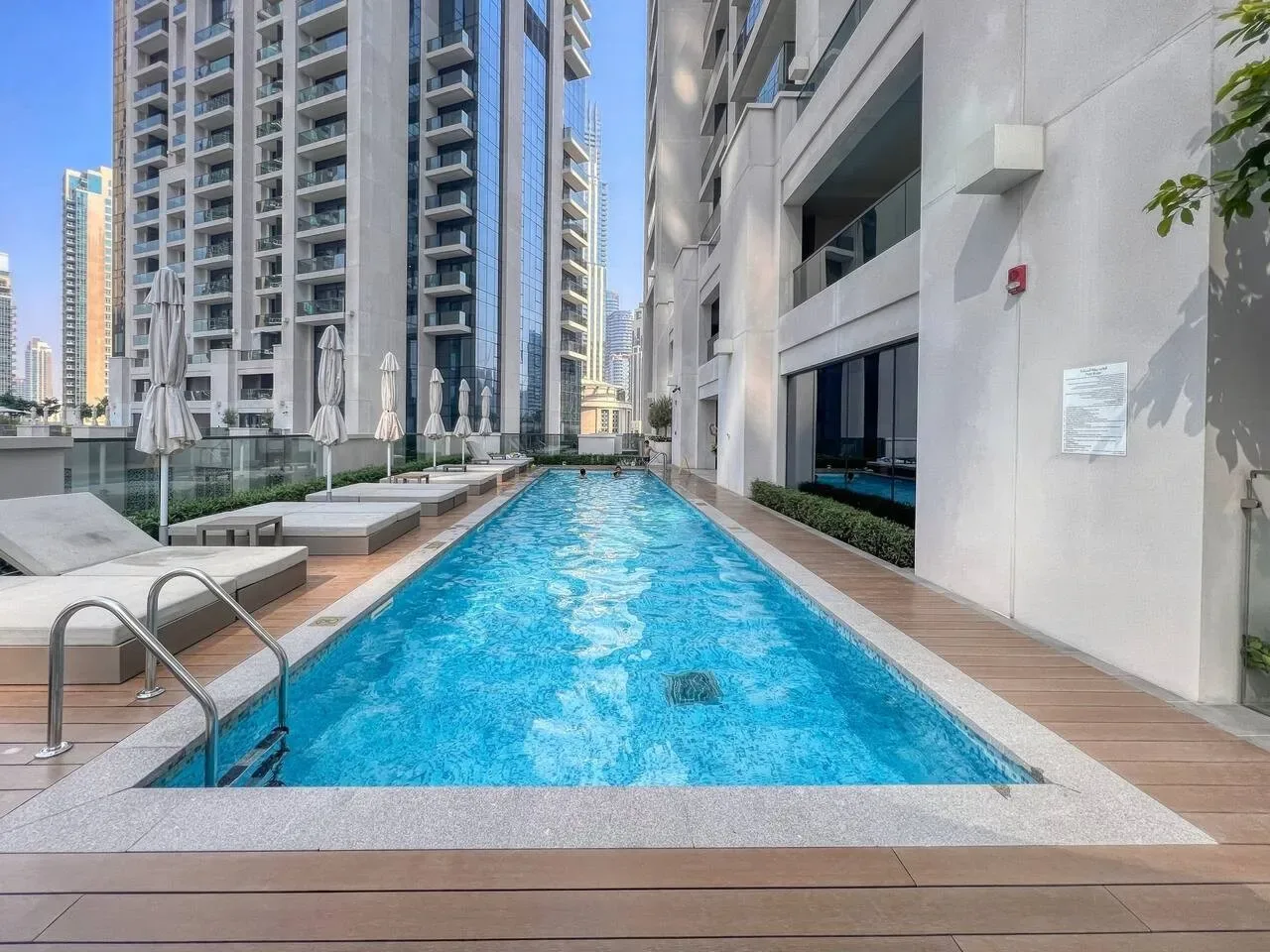 Una piscina al aire libre se extiende entre edificios altos modernos, con asientos junto al borde.