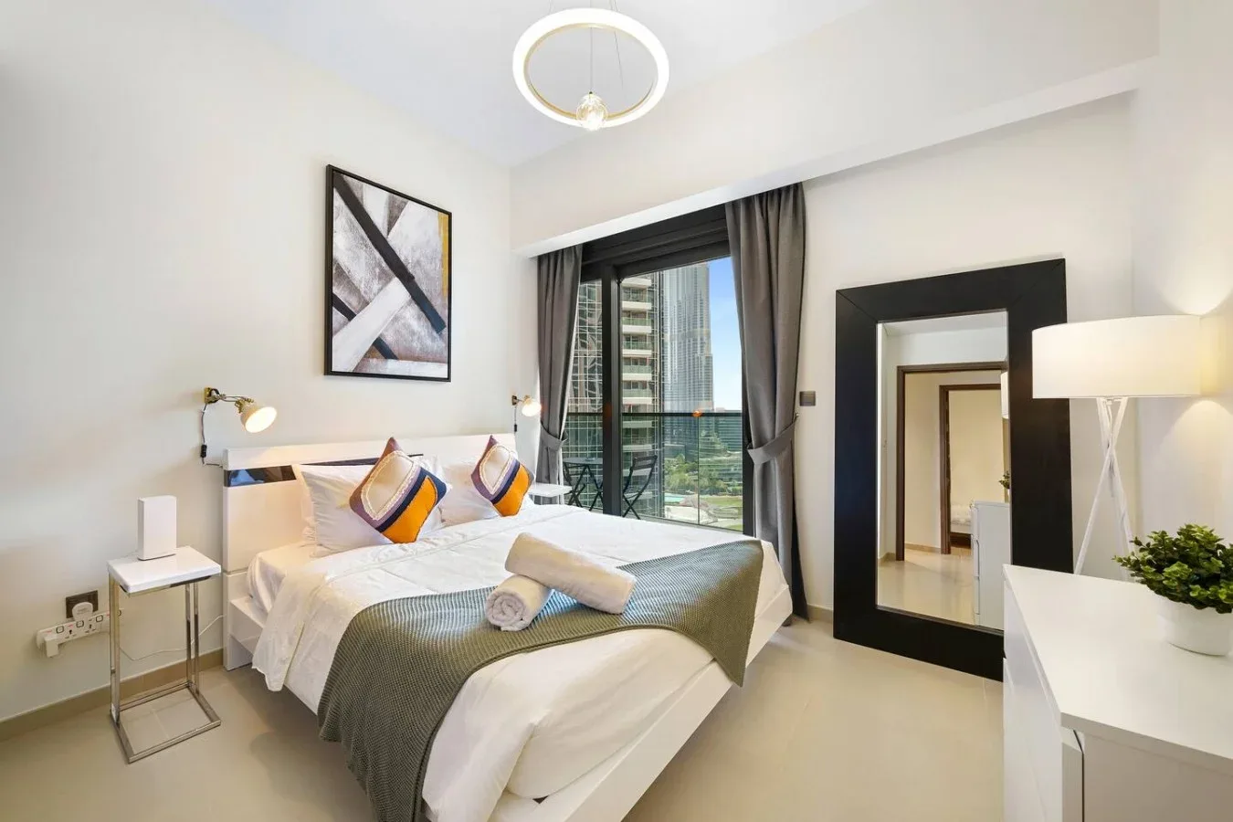 A bright bedroom with a neatly made bed and glass doors opening onto a balcony.