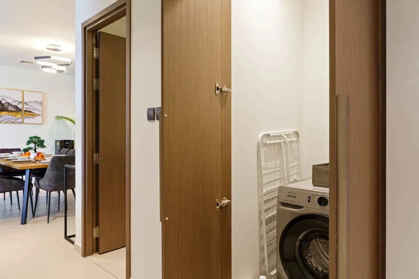 A hallway with open wooden doors reveals a washing machine and a dining area.