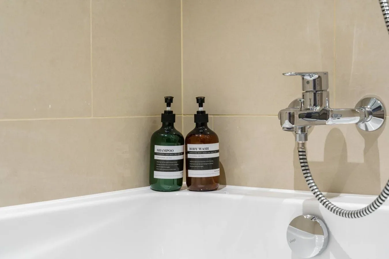 A bathtub and wall-mounted shower fixture are set against beige tiled walls.