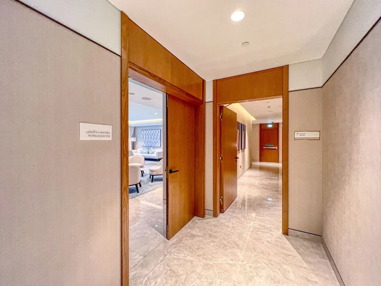 A bright hallway with tiled flooring and open wooden doorways.