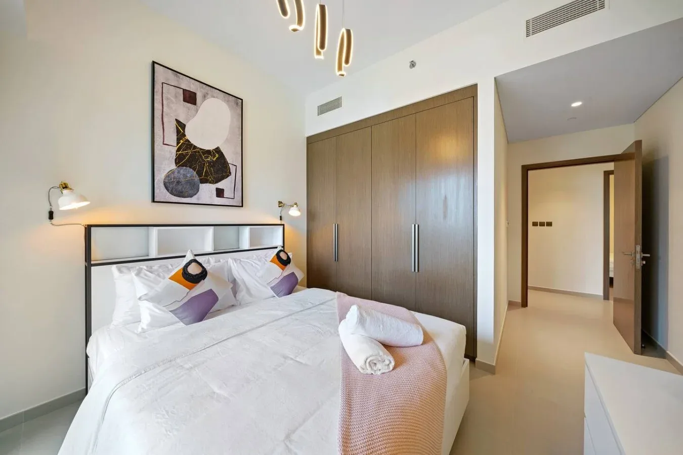 A bedroom with a neatly made bed and a large wooden wardrobe.