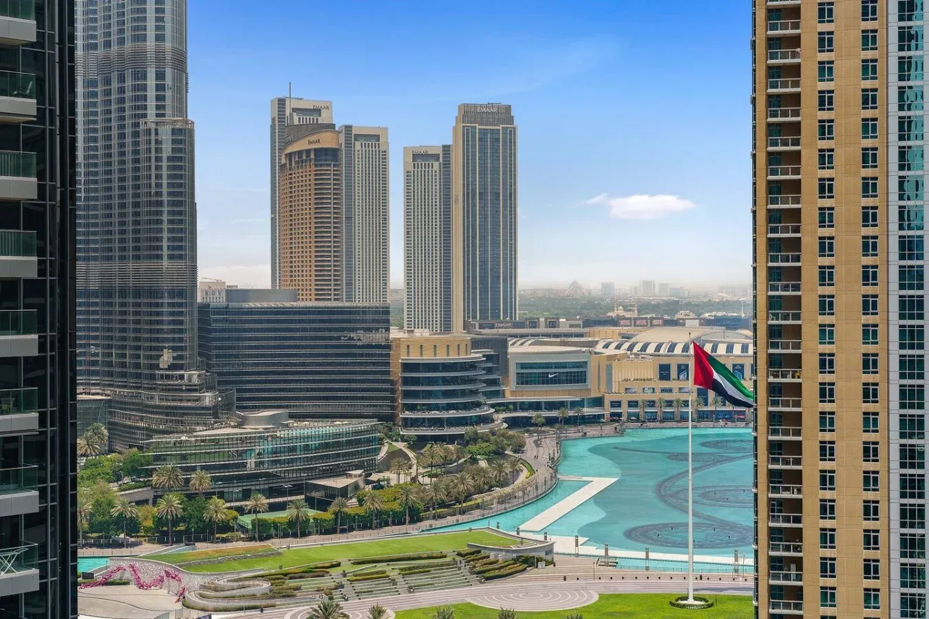 A city skyline overlooks a turquoise pool and landscaped grounds.