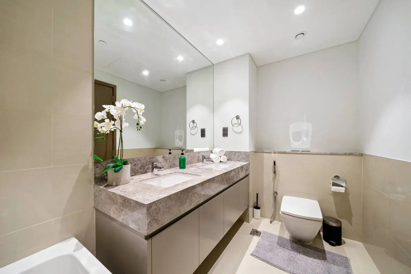 A bright bathroom with a long vanity, wall mirror, and toilet.