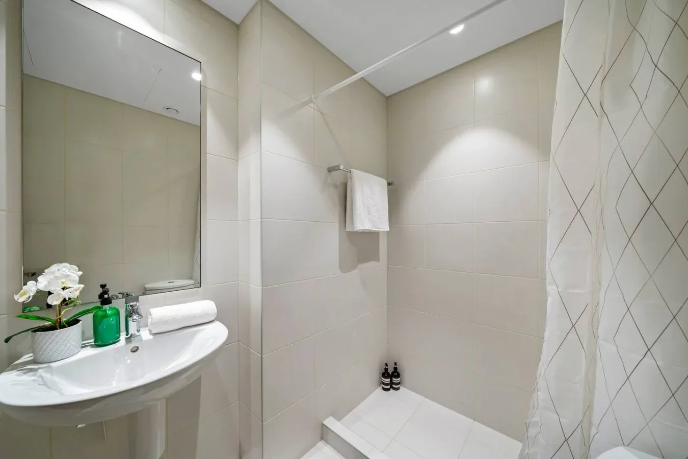 A tiled bathroom with a sink, mirror, and shower area.