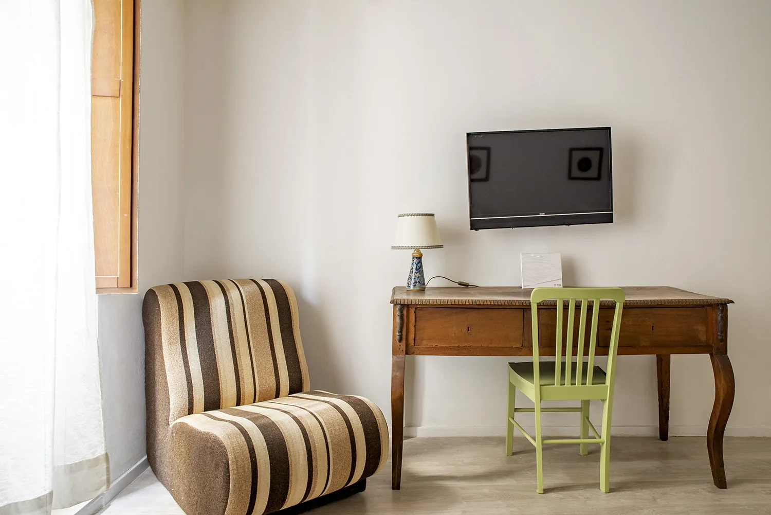Una habitación amueblada con un asiento a rayas junto a un escritorio de madera y una silla verde.