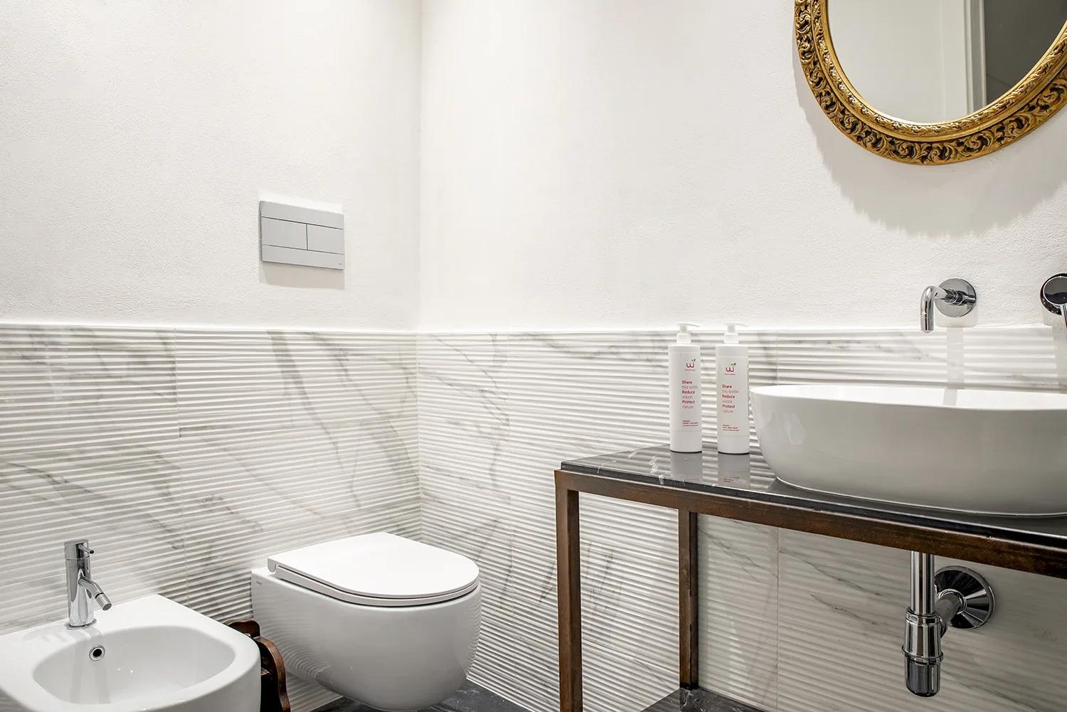 Un baño con lavabo, inodoro y una pila sobre la encimera bajo un espejo redondo.