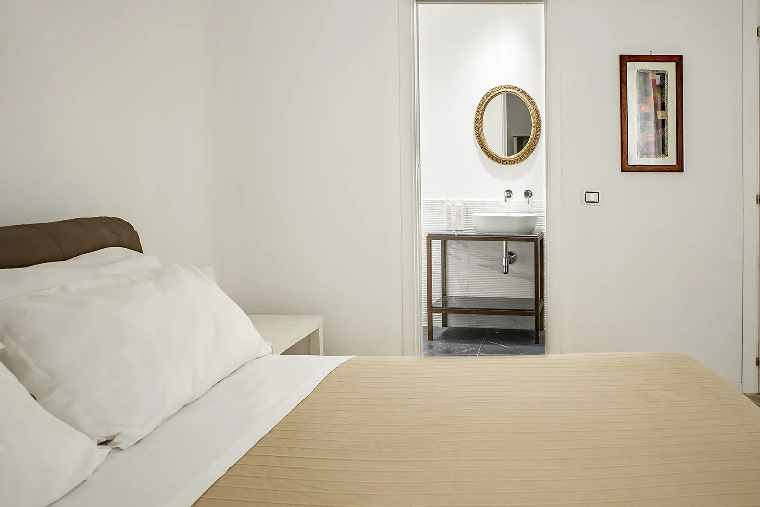 Un dormitorio con una cama bien hecha y un lavabo visible a través de la puerta.
