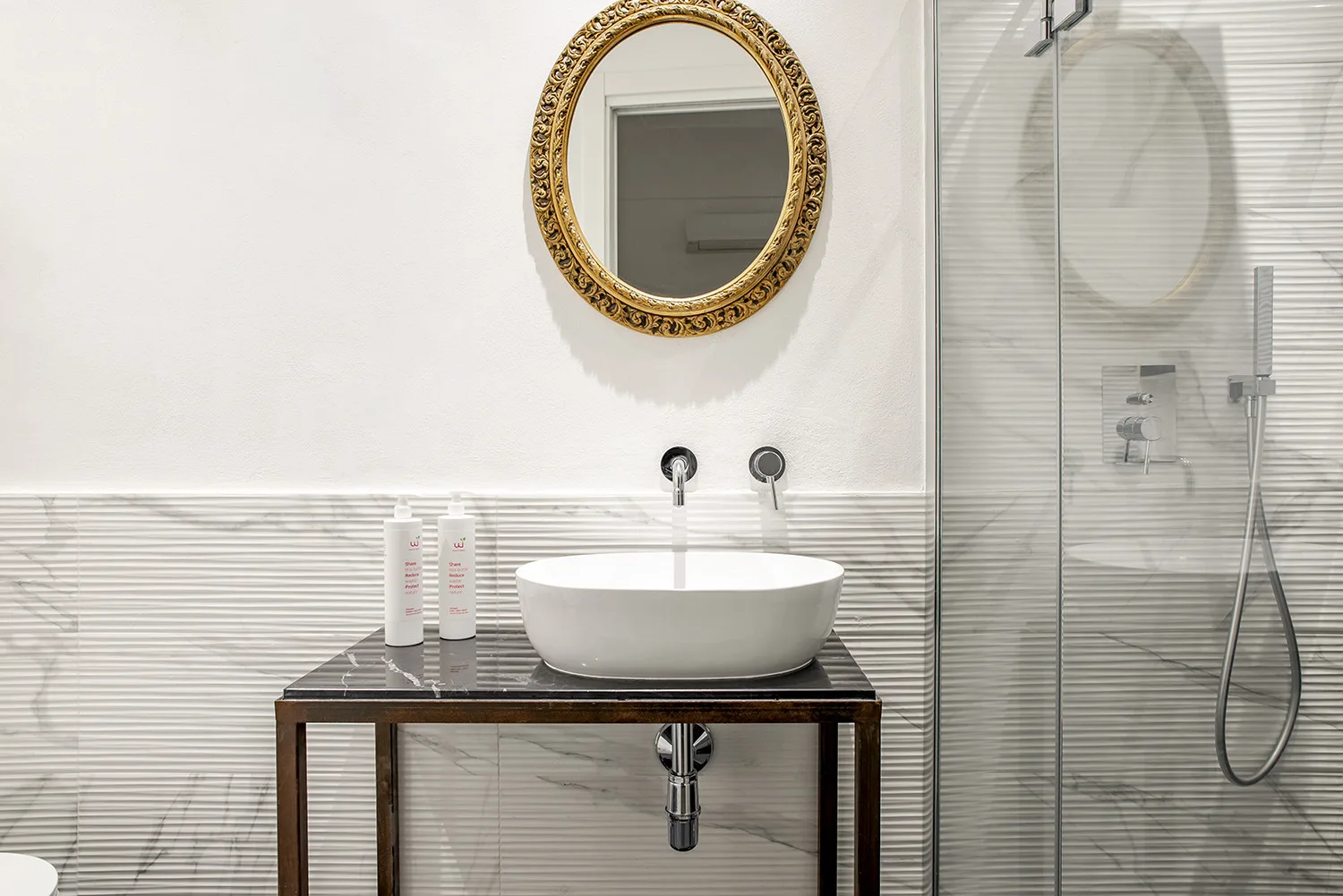 Un lavabo de baño con un lavamanos sobrepuesto y una ducha contigua.