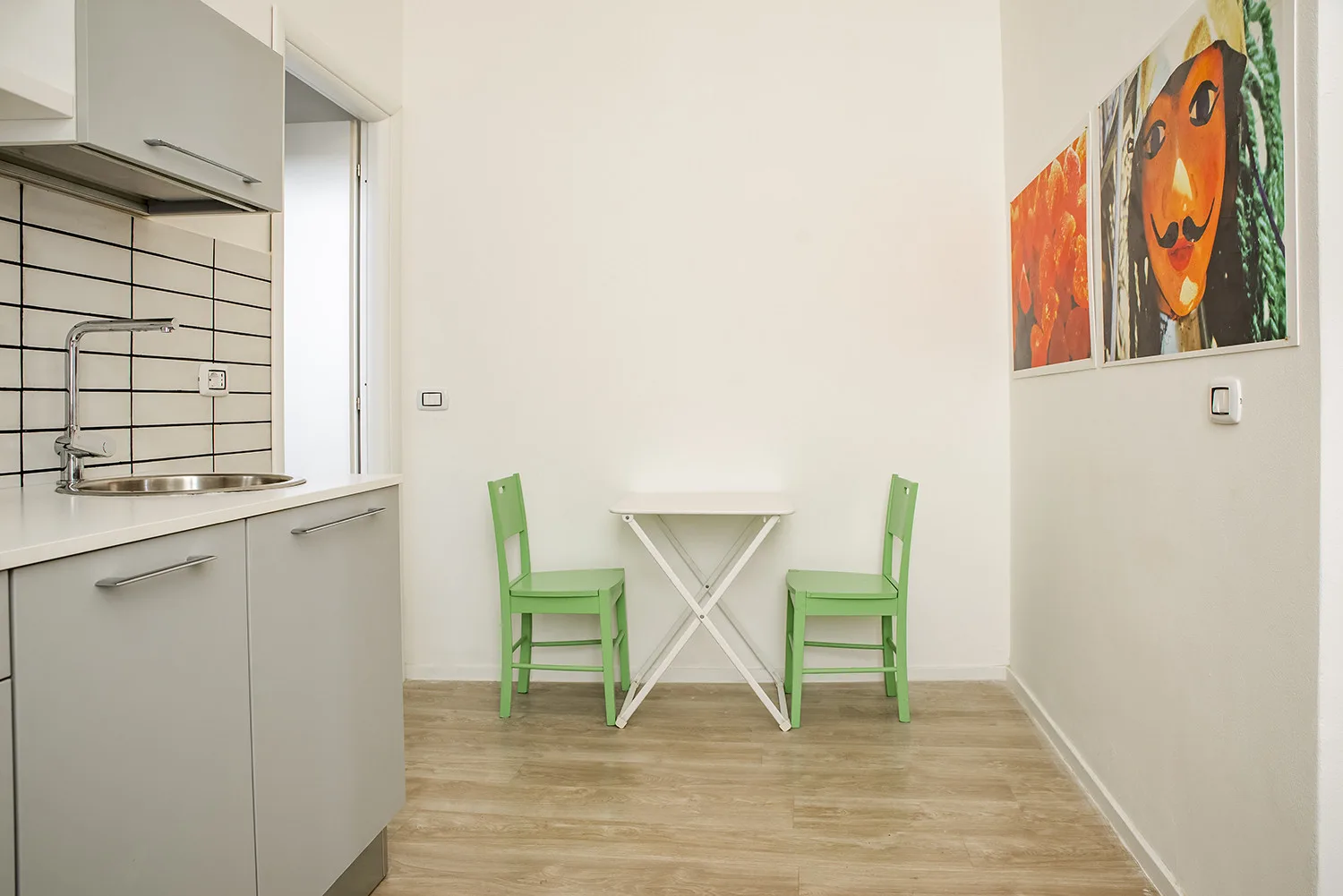 Una pequeña cocina y zona de comedor con sillas verdes junto a una mesa blanca.