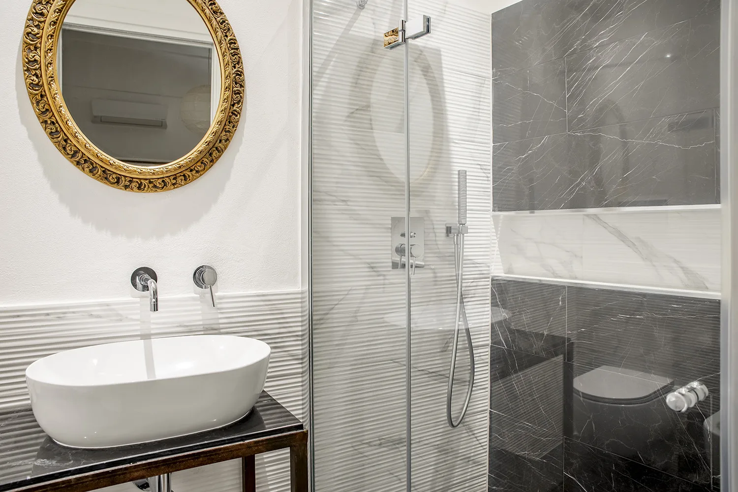 Un baño moderno con lavabo de recipiente, espejo ornamentado y ducha de vidrio.