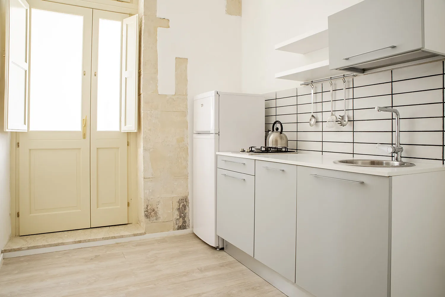 Una cocina luminosa con armarios blancos, salpicadero de azulejos y una ventana grande.