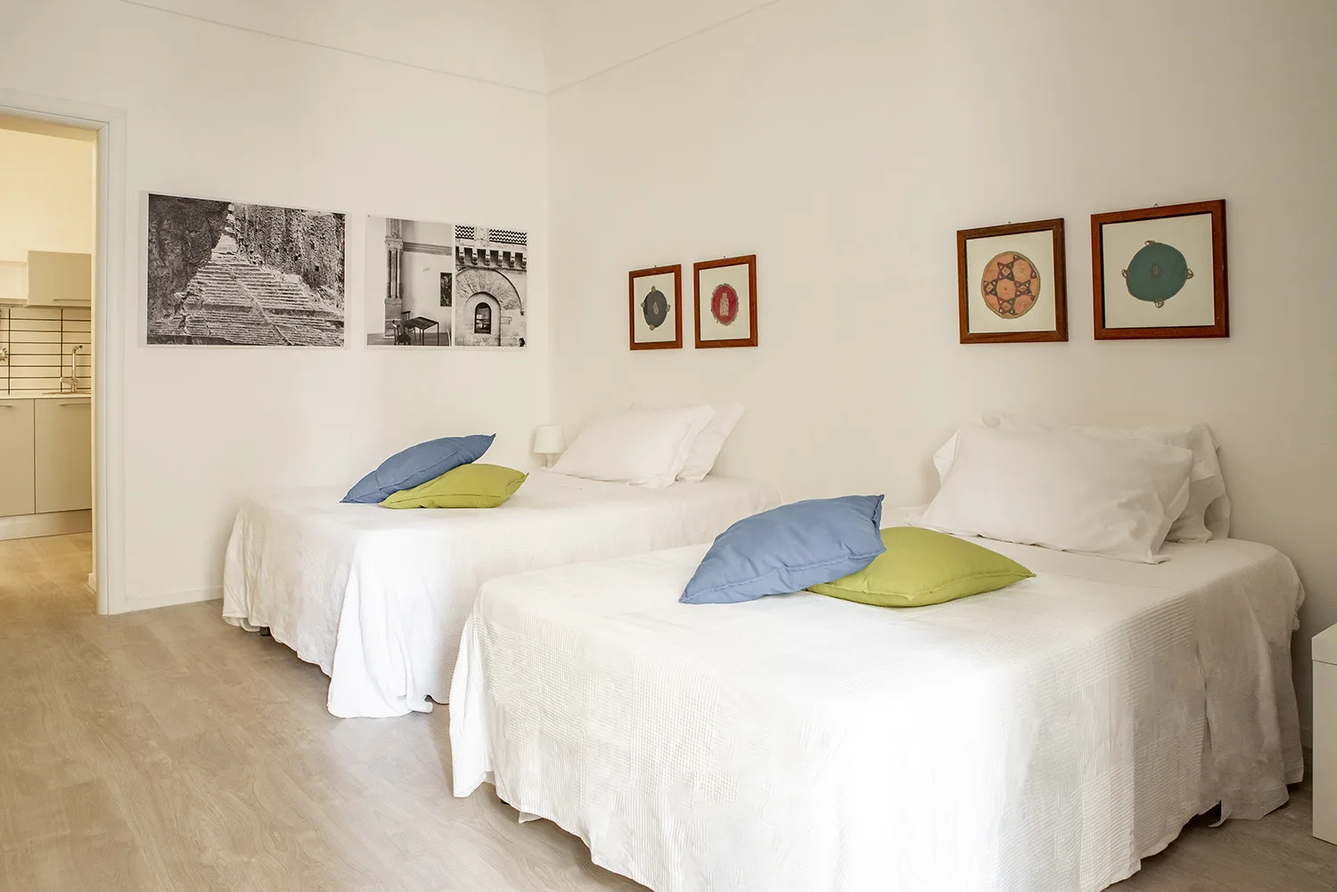 Un dormitorio luminoso con dos camas vestidas de blanco y cojines de colores.