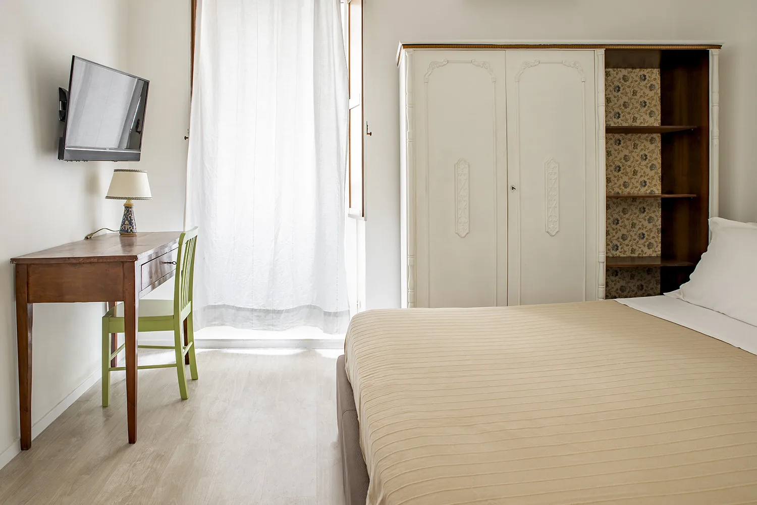 Dormitorio con cama, armario y escritorio junto a una ventana luminosa con cortinas.