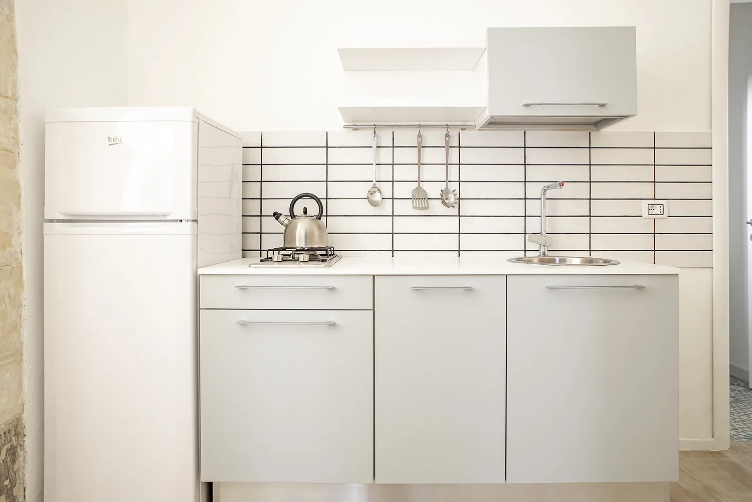 Una cocina blanca y luminosa con refrigerador, estufa y fregadero.