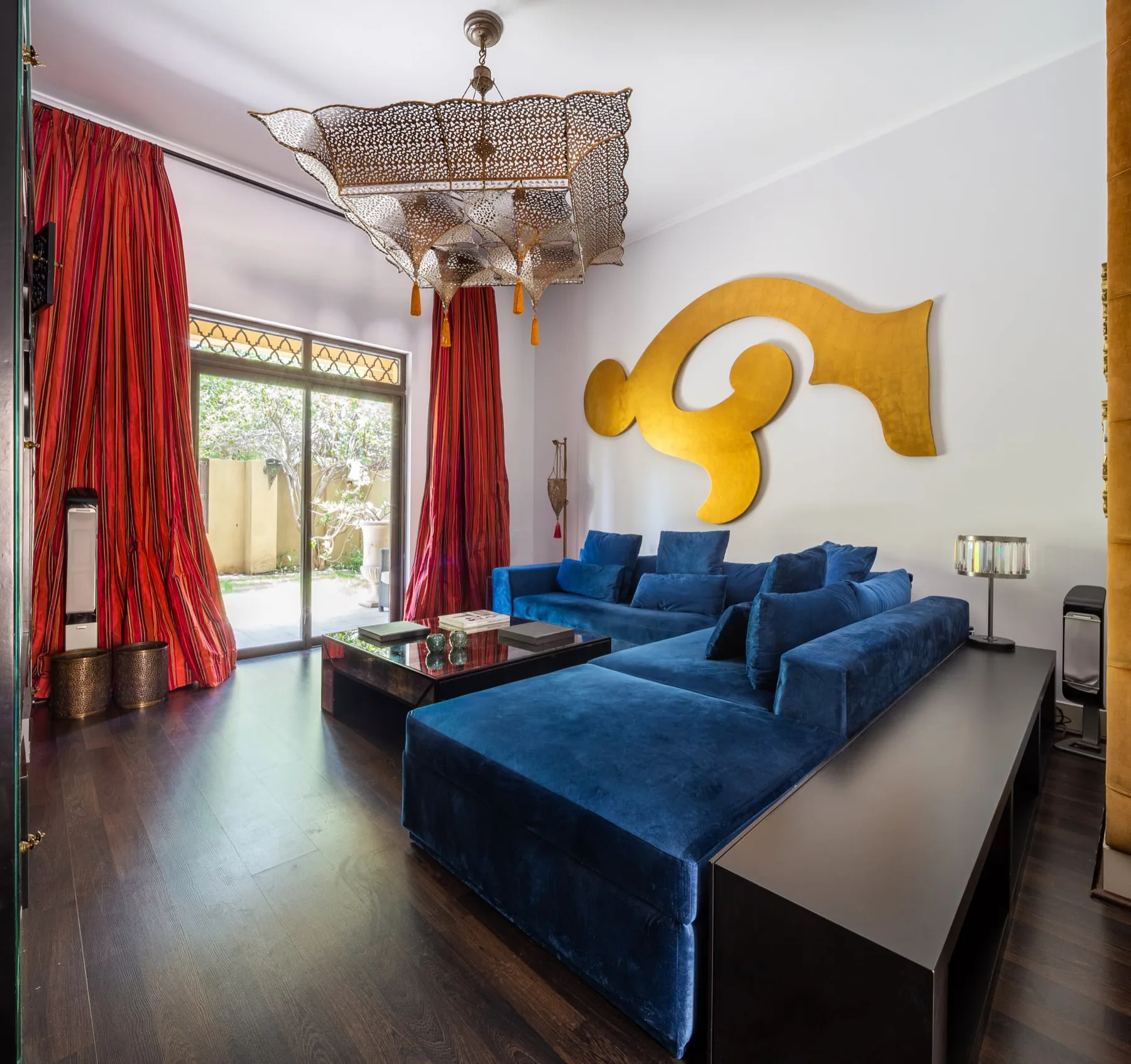 Una sala de estar con asientos azules, cortinas rojas y una gran escultura dorada en la pared.