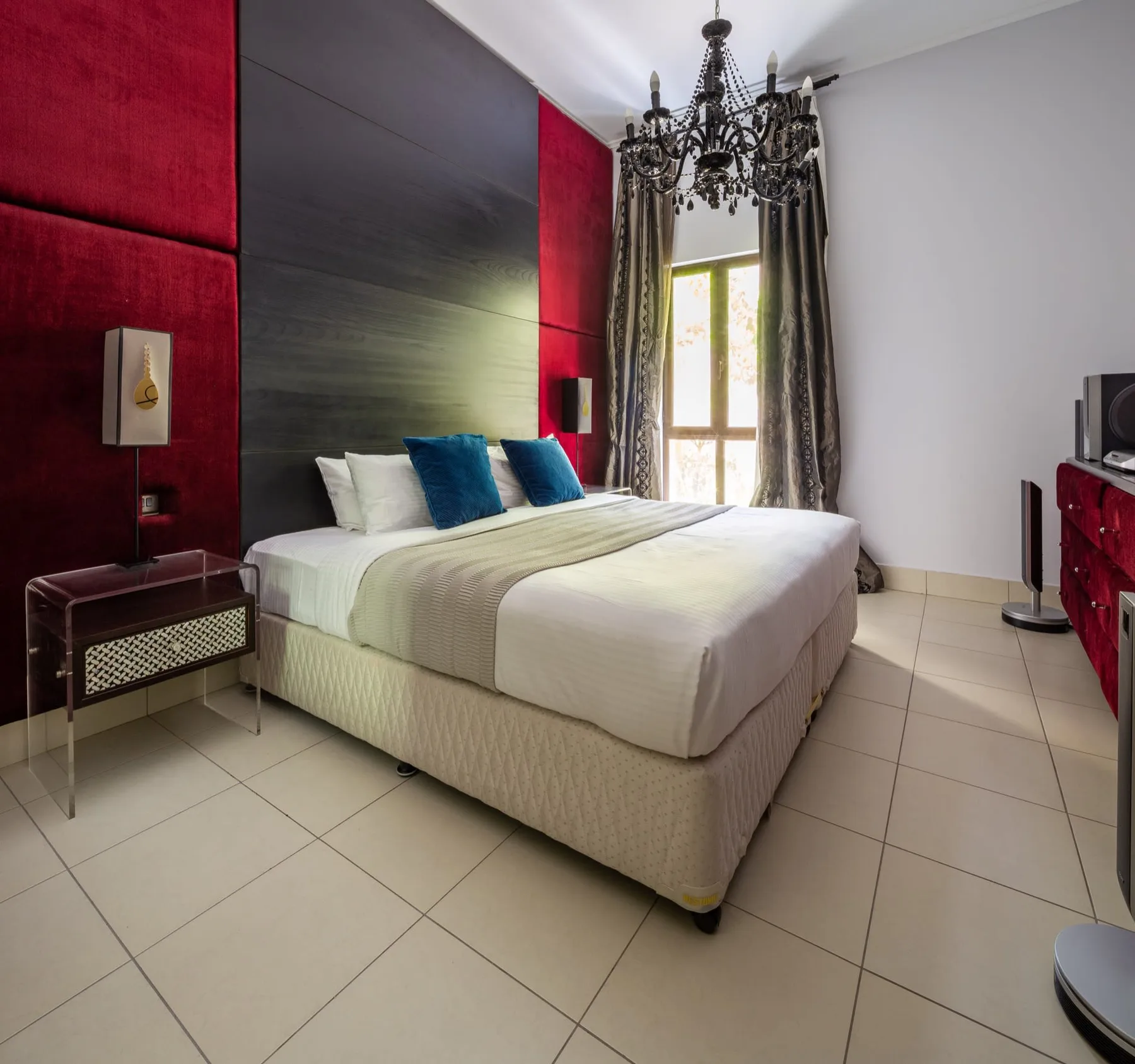 Un dormitorio con una cama bien tendida y ventanas altas con cortinas.