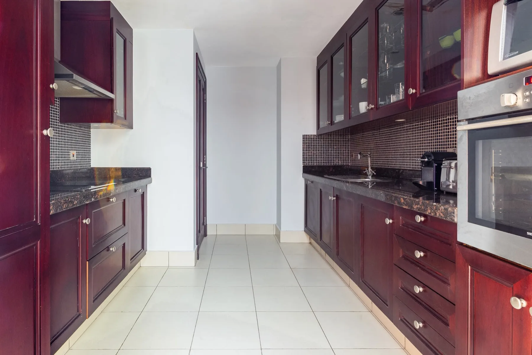 A narrow kitchen with dark cabinetry, tiled backsplash, and a central walkway.