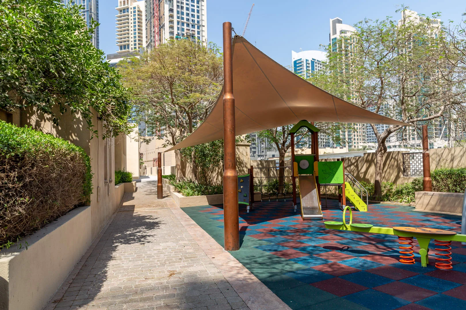 A shaded outdoor playground with colorful rubber flooring and play equipment.