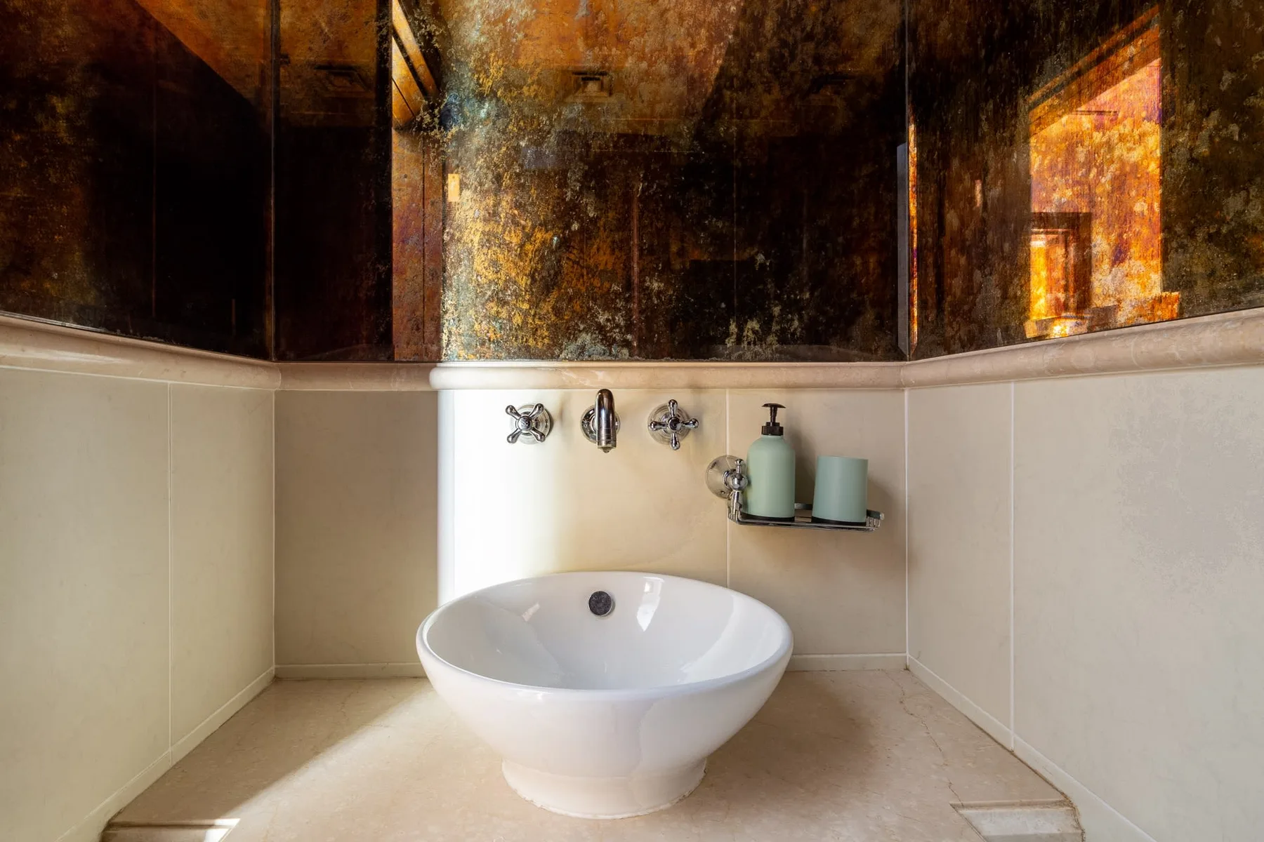 A bathroom sink sits beneath a large mirror, with toiletries on a small shelf.