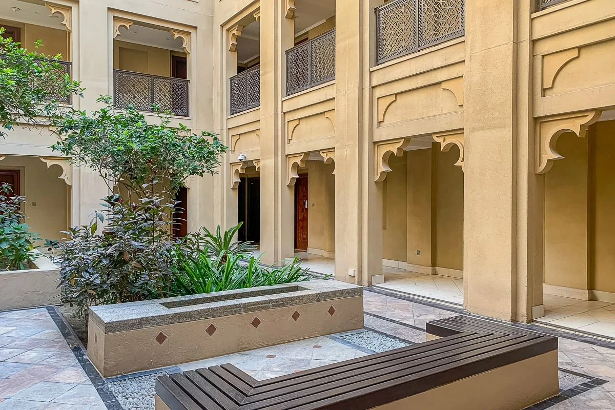 An open courtyard with arched walkways, planted greenery, and a built-in bench.