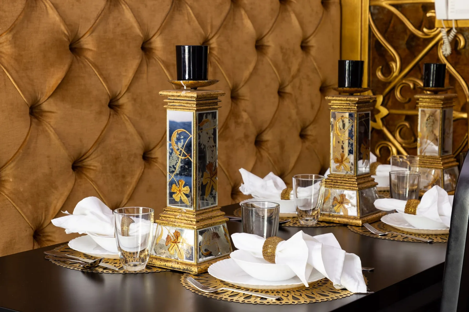 A dining table is set with white napkins and ornate decorative candleholders.