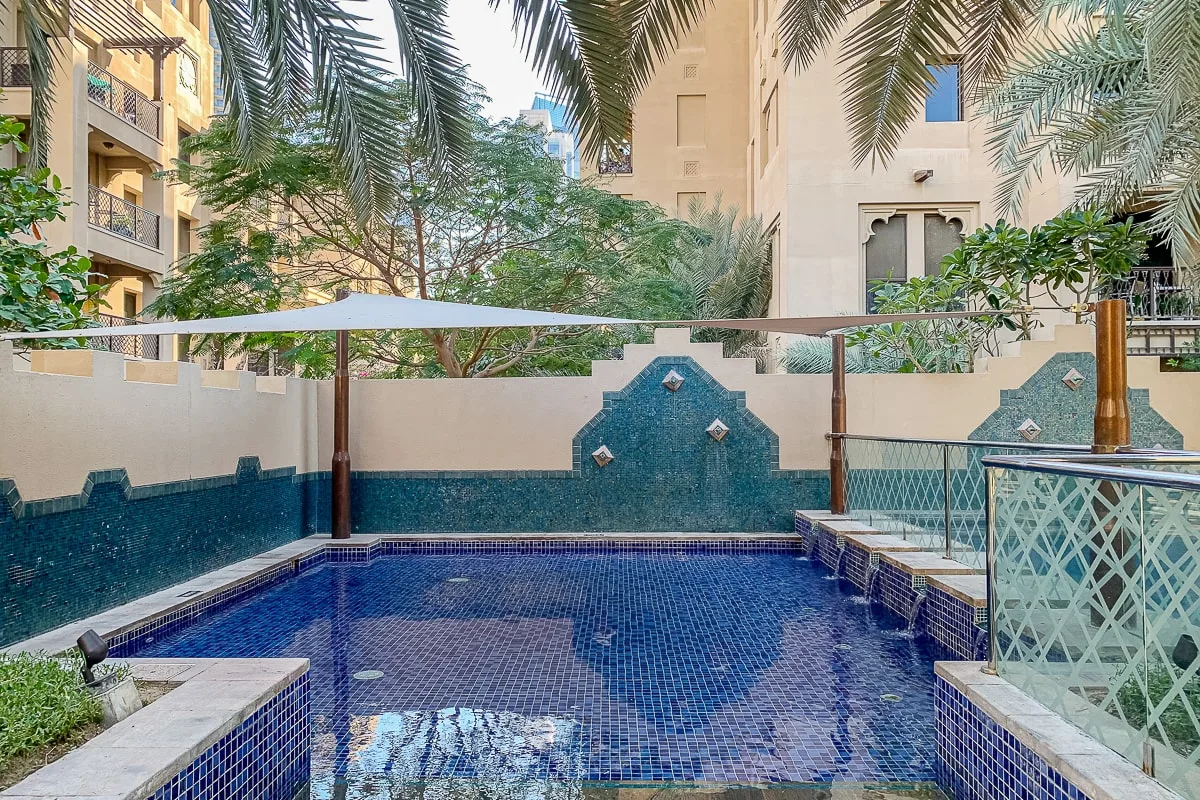 A small outdoor swimming pool sits beside a tiled wall and glass railing.